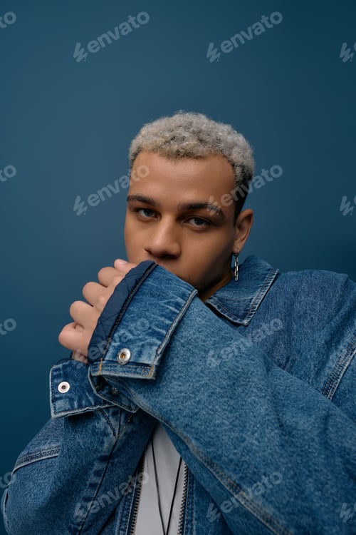 Preview: Stylish young man with dyed hair poses confidently against a vibrant blue backdrop