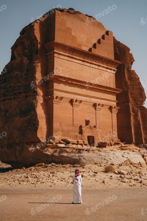 Preview: Vertical shot of a man standing in front of the Tomb of Lihyan son of Kuza in Saudi Arabia