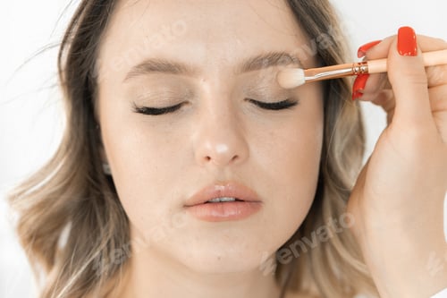 Preview: Charming face young woman is displayed in photo while applying makeup in beauty salon. Makeup artist