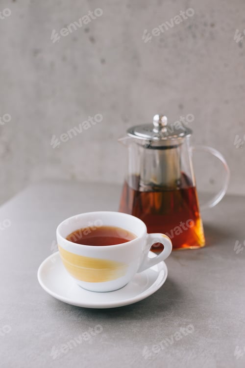 Preview: Glass teapot and cup with aromatic tea isolated on gray background.