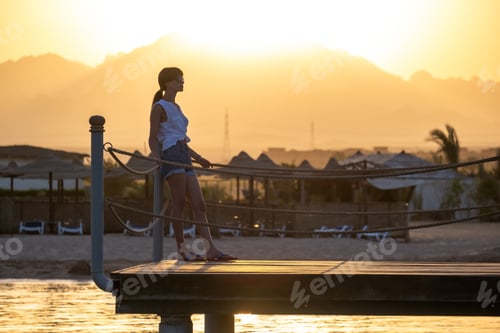 Preview: Happy woman relaxing outdoors on hotel deck on sea shore enjoying warm tropic evening