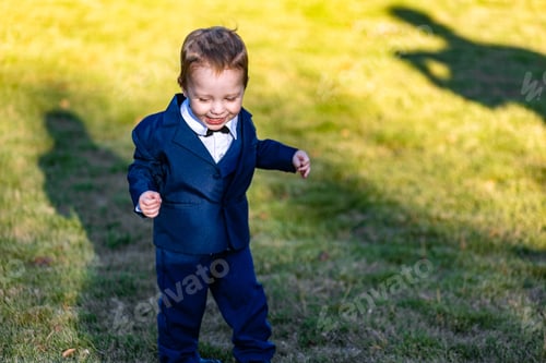 Preview: a young boy in a suit holding his shadow by the grass