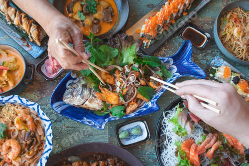 Preview: hands with chopsticks eating thai food close up, salads and wok, asian food, top view.