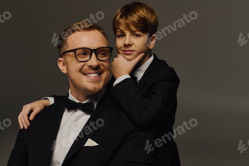 Preview: Handsome father and son showcase elegance in matching tuxedos at a stylish studio
