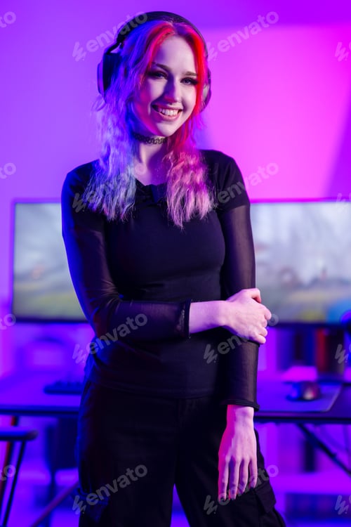 Preview: Portrait of a smiling e-sport gamer girl in front of her computer in her colorful gaming room