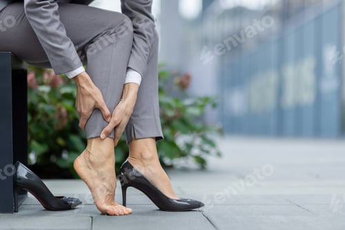 Preview: Businesswoman in pain, holding ankle on city street