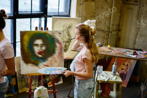 Preview: Caucasian artist with palette for mixing colors listening calm music playlist during art workshop in