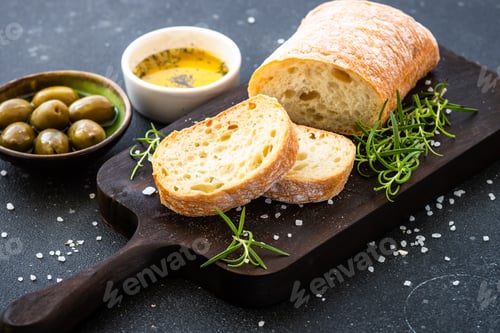 Preview: Ciabatta bread on wooden board with olive oil, olives and herbs.