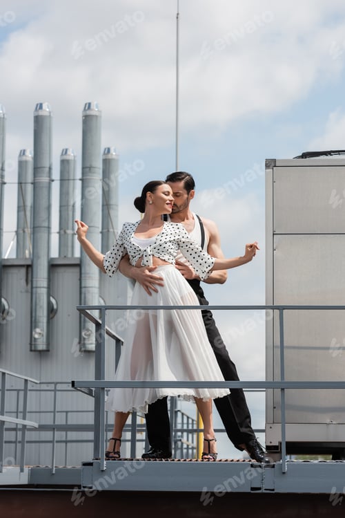 Preview: Stylish dancer hugging smiling partner while dancing on roof of building outdoors