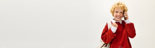 Preview: Cheerful child talks on phone while wearing stylish red sweater and backpack in school setting