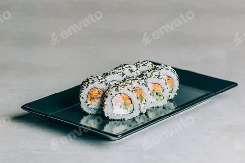 Preview: sushi rolls in sesame with salmon on black plate on gray background