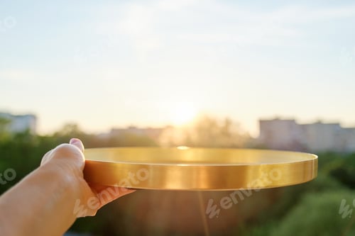 Preview: Round golden brass metal tray in womans hands, background sunset