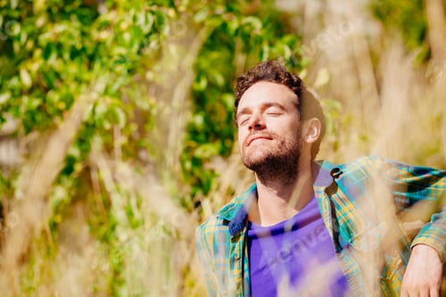 Preview: Mid adult man sitting in tall grass eyes closed basking in sunlight