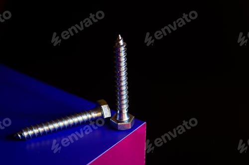 Preview: hardware, bolts, screws, self-tapping screws on the edge of a purple-pink cube on a black photo