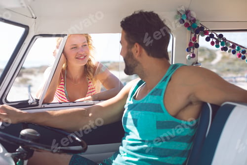 Preview: Caucasian man in camper van talking with woman while woman standing outside the van at beach