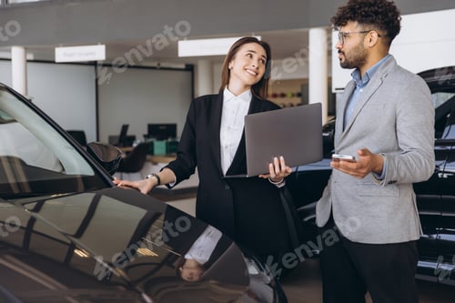 Preview: Saleswoman showing new car to customer in dealership