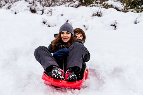 Preview: two very happy caucasian kids playing in the snow on a mountain with a red sled