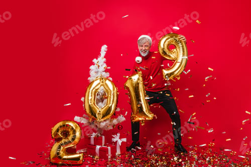 Preview: Adorable old man posing with new year presents and laughing. Santa claus dancing on red background