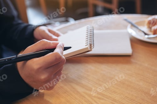 Preview: a woman holding and writing on blank notebook with coffee cup and croissant on table in cafe