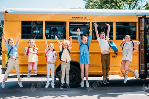 Preview: group of happy pupils jumping in front of school bus and looking at camera