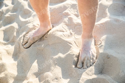 Preview: Bare feet and ankles of young man standing on dry sandy beach