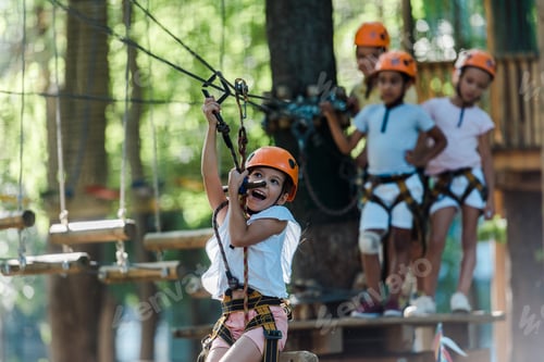 Preview: selective focus of excited kid riding on high rope trail near multicultural children