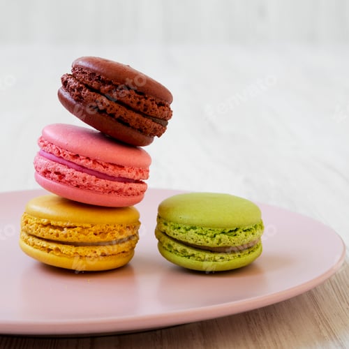 Preview: Colorful macarons on a pink plate over white wooden background, side view. Closeup.