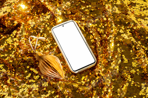 Preview: Smartphone with blank screen on sparkling gold sequin background with Christmas ornament.