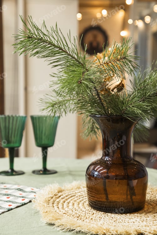 Preview: Christmas decor on the table. Vase with fir branches and glasses with lights on the background