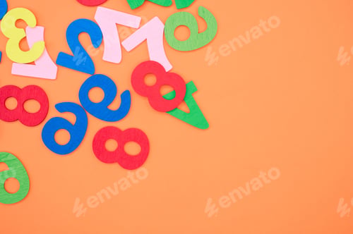 Preview: Flat lay of colorful wooden numbers scattered on an orange surface - space for text