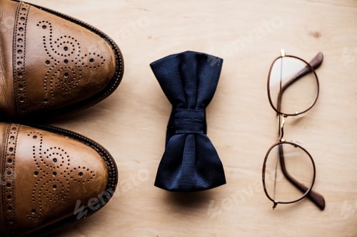 Preview: top view of shoes, tie bow and glasses on wooden surface