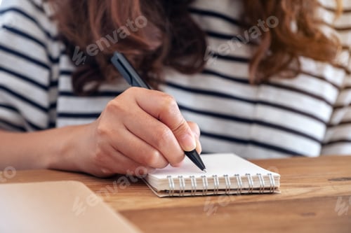 Preview: Closeup image of a woman writing on blank notebook and books on wooden table while learning