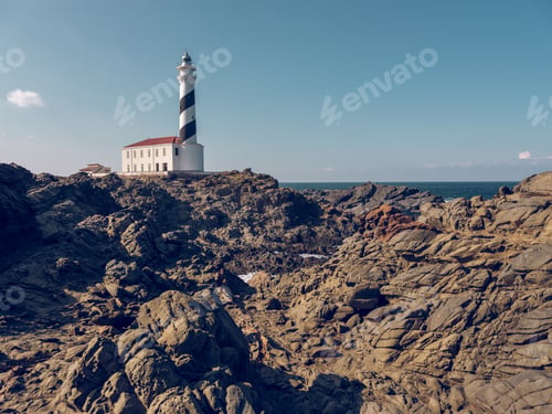 Preview: White lighthouse located on rocky coastline of ocean