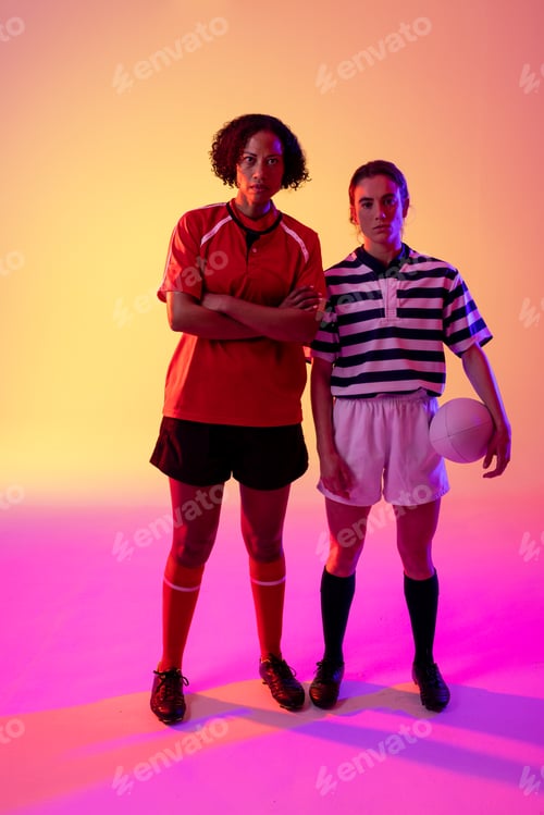 Preview: Portrait of two diverse female rugby players with rugby ball over neon pink lighting
