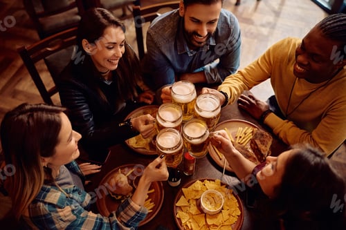 Preview: Multiracial group of happy friends toasting with beer in a bar.