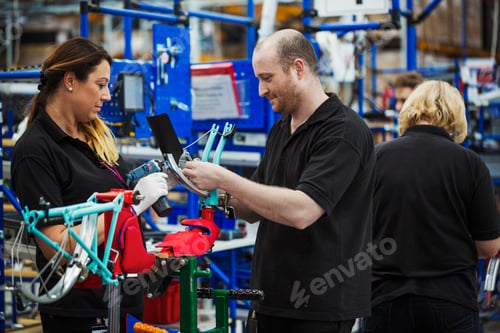 Preview: Three cycle factory workers, two women and a man assembling a bicycle in a factory.