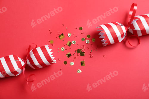 Preview: Open Christmas cracker with shiny confetti on red background, top view