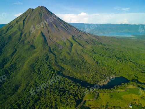 Preview: View of Arenal Volcano surrounded by lush green forest and a clear blue sky in Costa Rica