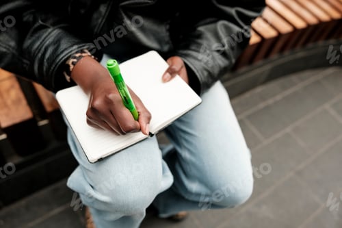 Preview: Black person writing notes in a small journal