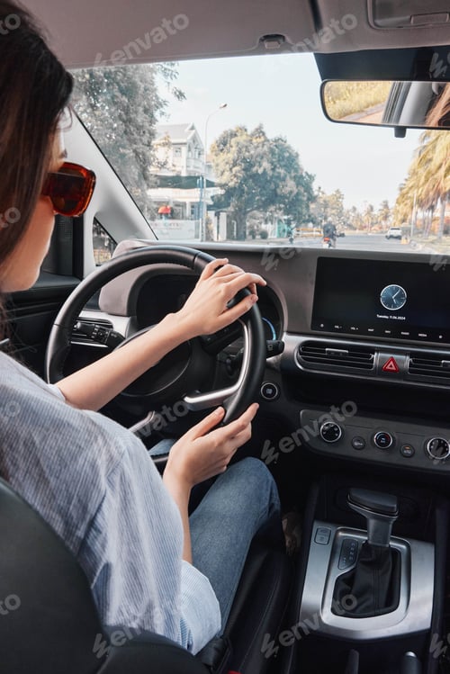 Preview: Woman driving car, hands on steering wheel, eyes on infotainment screen, focused and engaged, modern