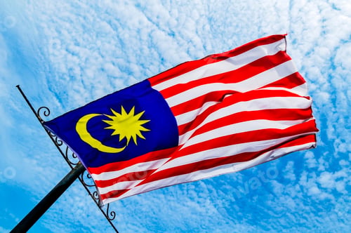 Preview: Low-angle view of the flag of Malaysia flying against blue sky