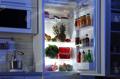 Preview: Open refrigerator full of products in stylish kitchen interior at night