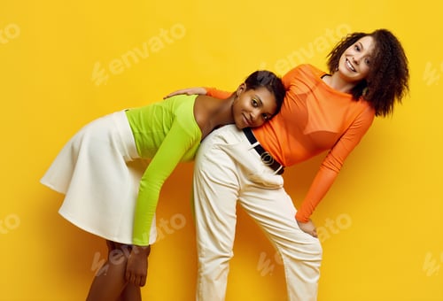 Preview: Portrait Of Two Young Beautiful Hipster Girls In Trendy Colorful Summer Clothes Isolated On Yellow