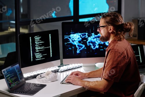 Preview: Young male programmer in eyeglasses looking at coded data on computer screen