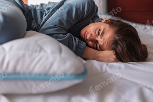 Preview: Curled up woman lying in bed having menstrual cramps