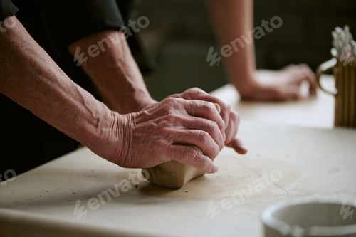 Preview: Senior Woman Kneading Clay on Table While Young Adult Assisting