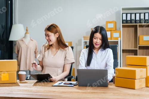 Preview: Two young female entrepreneurs work together in warehouse with parcel boxes, wooden tables shelves