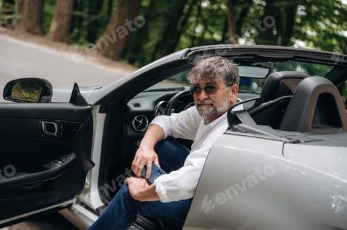 Preview: Door is opened, sitting and looking. Stylish senior man is in convertible cabriolet car