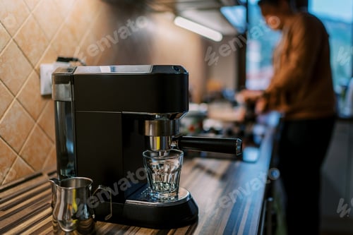 Preview: Empty glass stands on the stand of a carob coffee machine on a table against the background of a