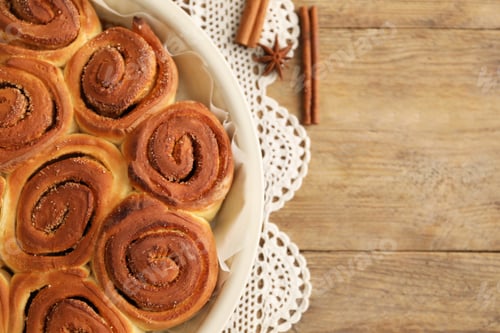 Preview: Freshly baked cinnamon rolls and spices on wooden table, flat lay. Space for text